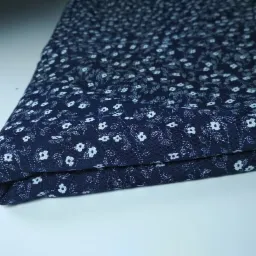 Złożony kawałek granatowej tkaniny w drobne białe kwiatki na białym tle.