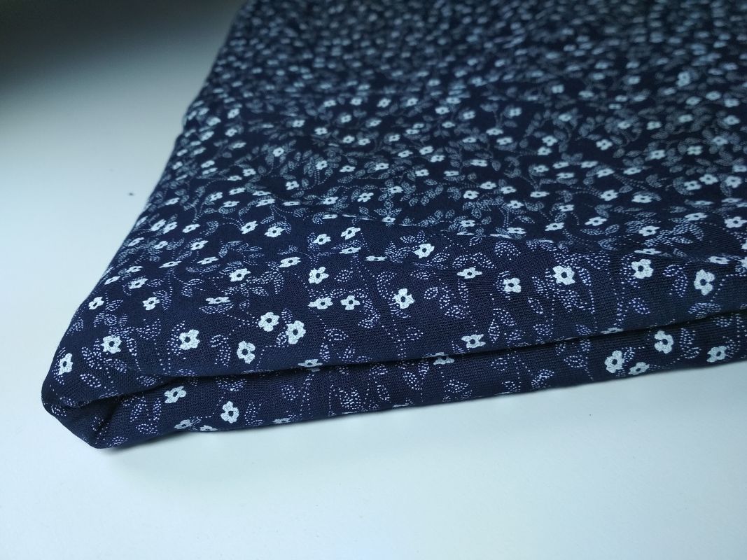 Złożony kawałek granatowej tkaniny w drobne białe kwiatki na białym tle.