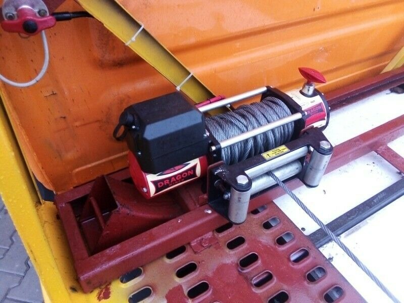 Elektryczna wciągarka marki Dragon zamontowana na platformie lawety, widoczny nawinięty stalowy kabel i elementy konstrukcyjne w kolorach żółtym, pomarańczowym i czerwonym.