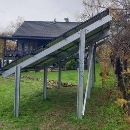 P.H.U. Eco-Constans - Montaż konstrukcji wsporczej pod panele fotowoltaiczne na trawniku przed domem jednorodzinnym, widoczny samochód serwisowy z otwartymi drzwiami.