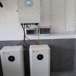 P.H.U. Eco-Constans - Biały inwerter Daye i dwa magazyny energii Felicity ESS zamontowane na ścianie w pomieszczeniu z szarą podłogą. Widoczne przewody i skrzynki elektryczne.