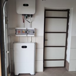 P.H.U. Eco-Constans - Biały magazyn energii Huawei z inwerterem i rozdzielnicą w garażu, widok z niskiej perspektywy. Instalacja przy ścianie z szarą glazurą, obok metalowe drzwi.