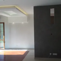 Wnętrze pokoju z ciemną ścianą z wnęką, otwartymi drewnianymi drzwiami balkonowymi i podwieszanym sufitem z oświetleniem LED.