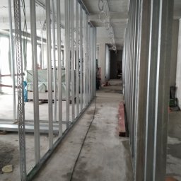 Polteam - Metalowa konstrukcja szkieletowa ścian działowych, widok wzdłuż korytarza w trakcie montażu, z widocznymi przewodami pod sufitem.
