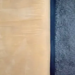 Fragment dywanu z widocznymi śladami po czyszczeniu, gdzie prawa strona jest szara i puszysta, a lewa jaśniejsza i bardziej gładka, oddzielone ciemnym pasem.