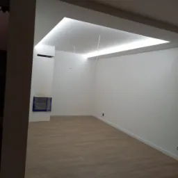 Pusty pokój z parkietem, świeżo pomalowanymi białymi ścianami i podwieszanym sufitem z oświetleniem LED, zabezpieczony otwór kominkowy folią.