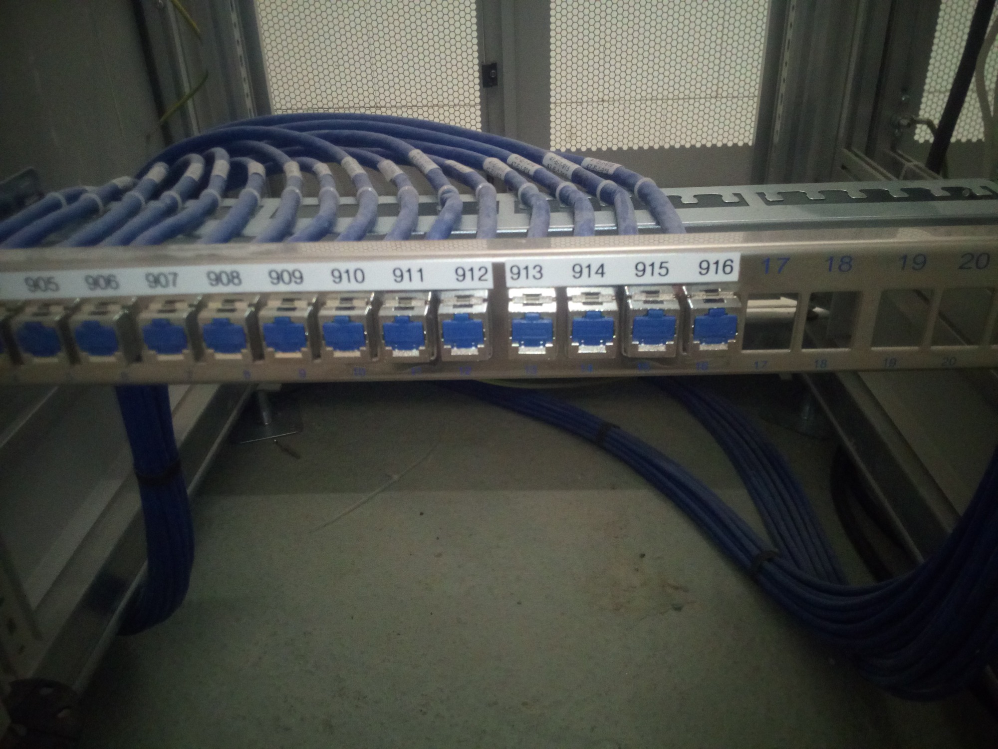 Panel krosowniczy z podłączonymi niebieskimi kablami sieciowymi, oznaczony numerami od 905 do 916 oraz 17 do 20, w szafie serwerowej.