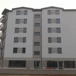 Nowo wybudowany, szary budynek wielorodzinny z balkonami, widoczny z zewnątrz, z przenośną toaletą na pierwszym planie.