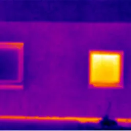 Termowizyjne zdjęcie elewacji budynku z dwoma oknami, gdzie jedno okno wykazuje znaczną utratę ciepła, zaznaczoną na żółto na skali temperatur po prawej stronie.