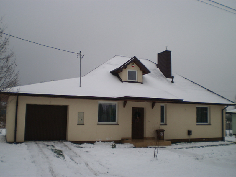 Dom jednorodzinny z garażem, otynkowany na beżowo, pokryty śniegiem, w pochmurny dzień.