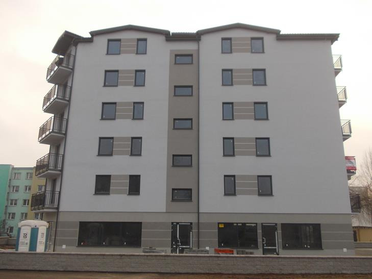 Nowo wybudowany, szary budynek wielorodzinny z balkonami, widoczny z zewnątrz, z przenośną toaletą na pierwszym planie.