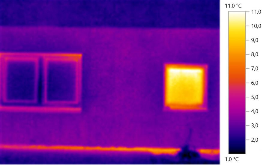 Termowizyjne zdjęcie elewacji budynku z dwoma oknami, gdzie jedno okno wykazuje znaczną utratę ciepła, zaznaczoną na żółto na skali temperatur po prawej stronie.