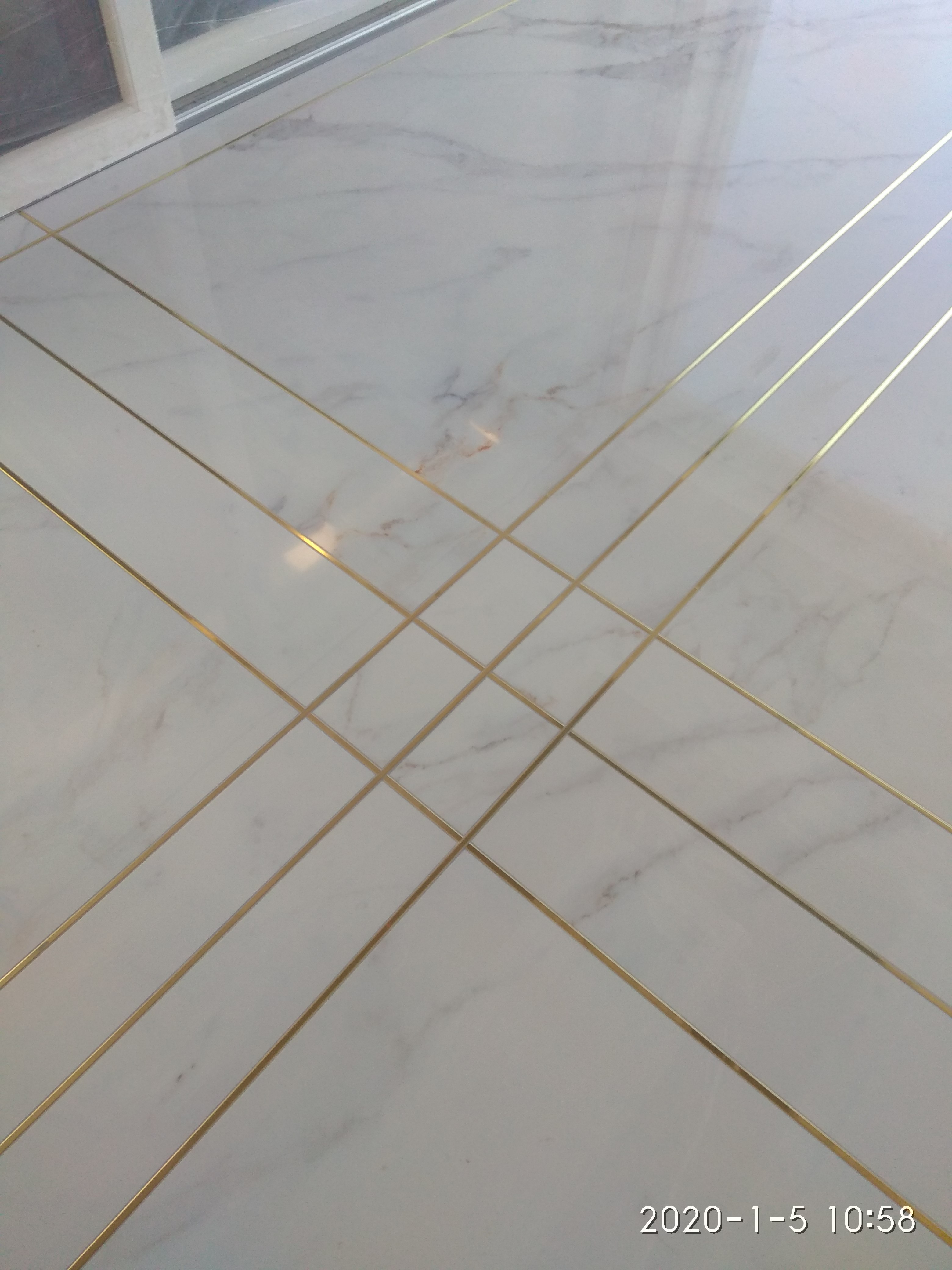 Wykończona podłoga z białych płytek imitujących marmur, z dekoracyjnymi złotymi listwami ułożonymi w geometryczny wzór.