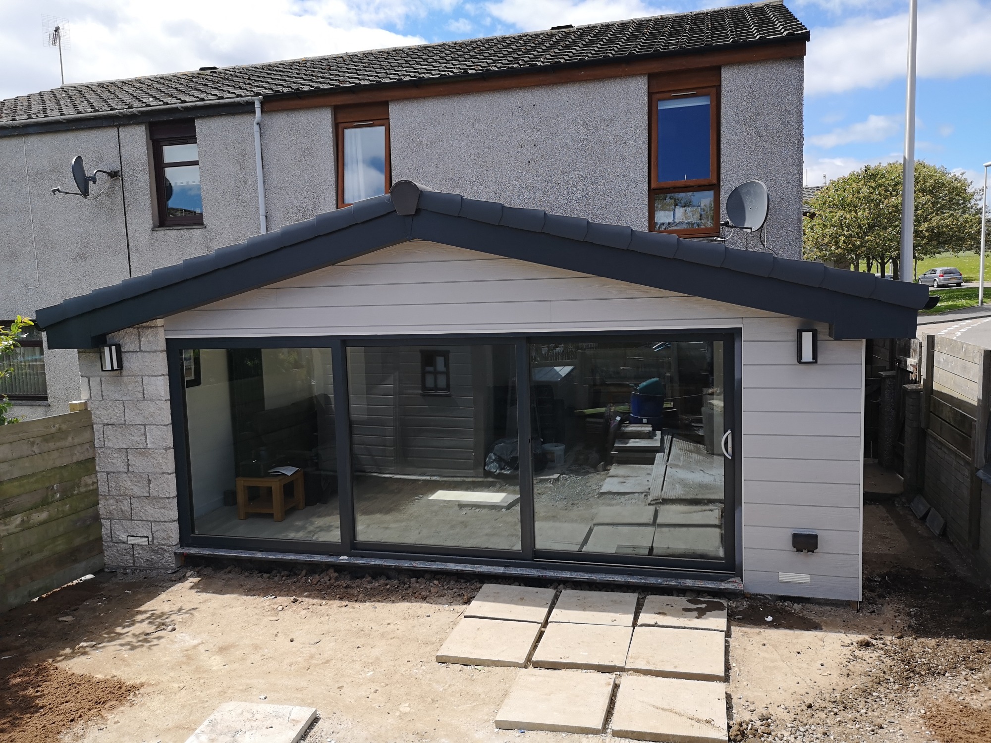 Dobudówka do domu z dużymi przesuwnymi oknami, wykończona szarym sidingiem i kamieniem, widok z zewnątrz, Gorzów Wielkopolski.