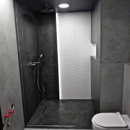 MAYKI Michał Ptaszek - Nowoczesna kabina prysznicowa z czarnymi marmurowymi płytkami i białą ścianą z falistym wzorem, widoczna toaleta podwieszana, minimalistyczny design.