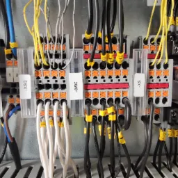 Panel sterowania z licznymi przewodami oznaczonymi żółtymi etykietami, podłączonymi do listew zaciskowych i przekaźników Schneider RXM 24 VDC.