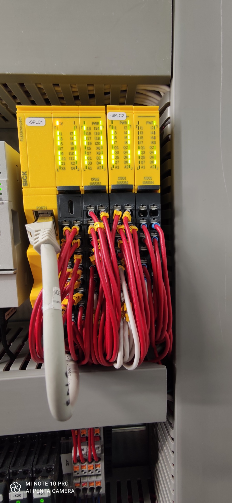 Panel sterowania z modułami SICK Flexi Compact, widoczne przewody w kolorze czerwonym i białym, podłączone do modułów, diody LED sygnalizujące pracę.