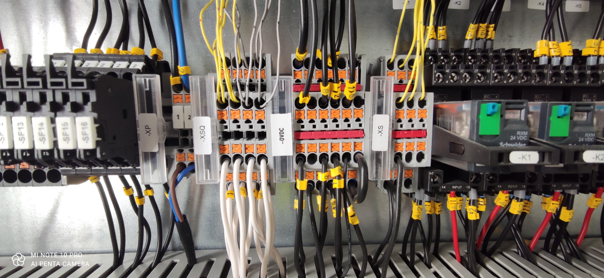 Panel sterowania z licznymi przewodami oznaczonymi żółtymi etykietami, podłączonymi do listew zaciskowych i przekaźników Schneider RXM 24 VDC.