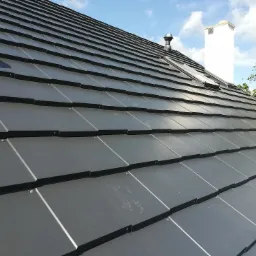 Nowoczesny, grafitowy dach z dachówki ceramicznej na budynku w Białej Podlaskiej, widoczny komin i okno dachowe, błękitne niebo w tle.