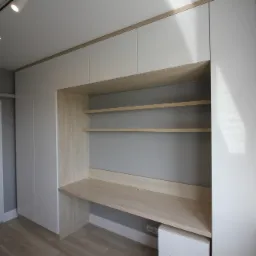 Biała zabudowa meblowa z biurkiem i półkami z jasnego drewna, zintegrowana ze ścianą, oświetlenie punktowe na suficie.