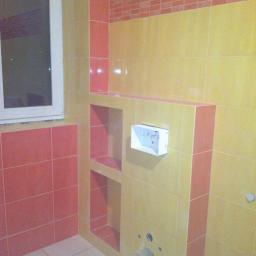 Zakład remontowo-budowlany - Wykończona łazienka z żółto-różowymi płytkami, wnękami w ścianie i przygotowanym miejscem na armaturę.