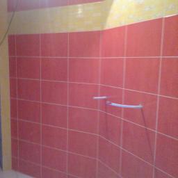 Zakład remontowo-budowlany - Ściana łazienki wyłożona różowymi płytkami z poziomym pasem żółtych płytek u góry i zamontowanym uchwytem na ręczniki.