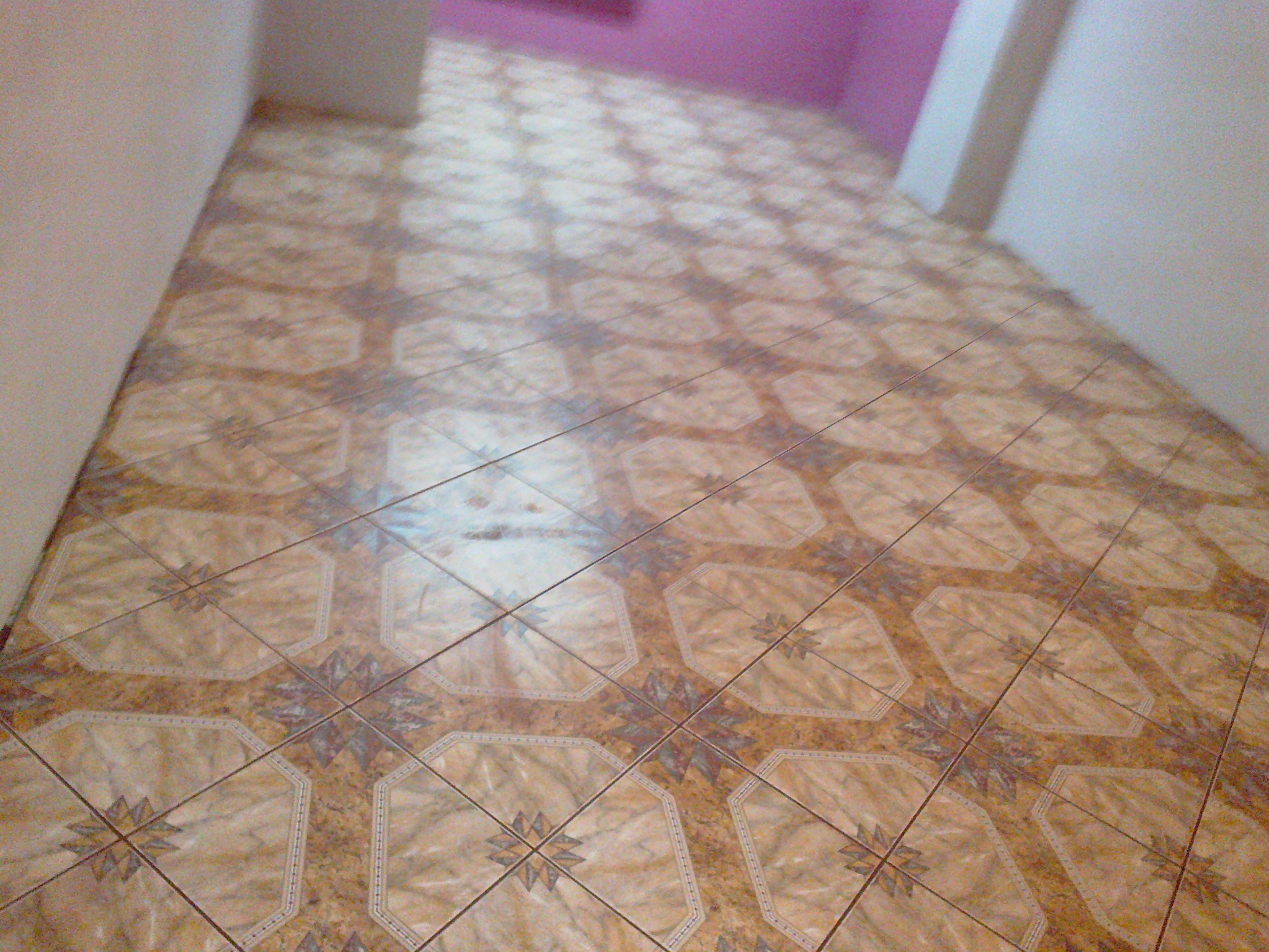 Ułożona podłoga z płytek ceramicznych w odcieniach beżu i brązu, wzór w kształcie gwiazdy, widok z perspektywy pod kątem, ściana pomalowana na różowo w tle.