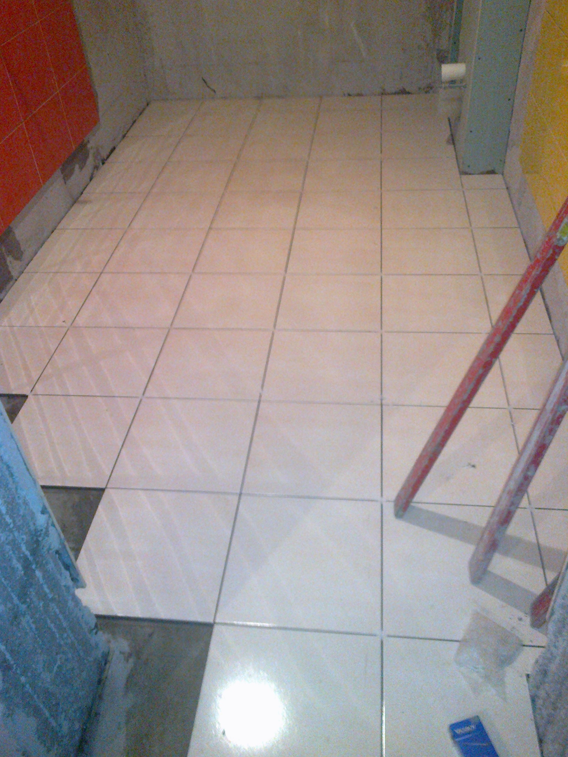 Układanie jasnych płytek podłogowych w trakcie prac w łazience w Kielcach, widoczna poziomica i częściowo wykończone ściany.