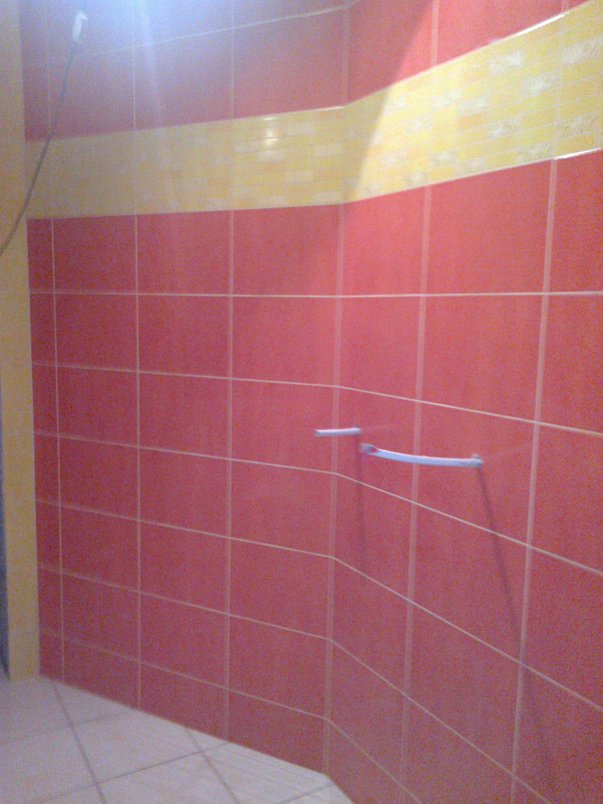 Ściana łazienki wyłożona różowymi płytkami z poziomym pasem żółtych płytek u góry i zamontowanym uchwytem na ręczniki.