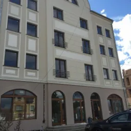 Elewacja budynku z zamontowanymi oknami i drzwiami w brązowych ramach, widoczny samochód z logo firmy na parkingu.