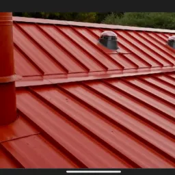 Błyszczący, czerwony dach z blachy trapezowej z kominem i wentylatorami dachowymi, widok z góry.