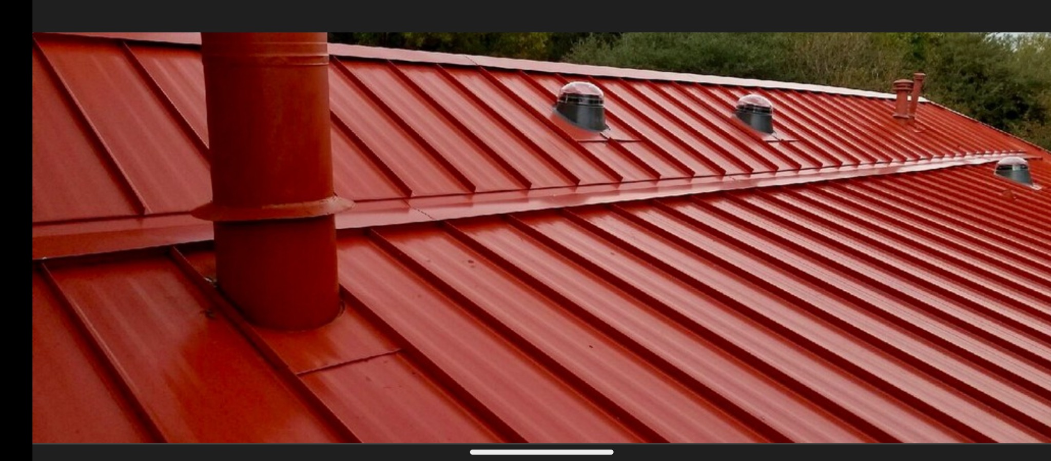 Błyszczący, czerwony dach z blachy trapezowej z kominem i wentylatorami dachowymi, widok z góry.