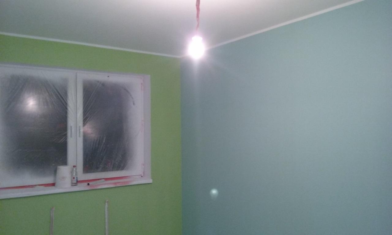 Pokój po odświeżeniu: ściany w dwóch odcieniach zieleni, okno zabezpieczone folią malarską, widoczny biały sufit i żarówka.