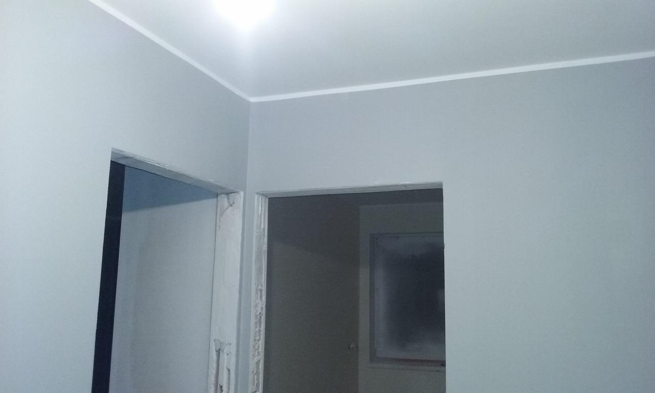 Świeżo pomalowane na szaro ściany z listwą w Trzebnicy. Widoczne dwa otwory drzwiowe, sufit i fragment ściany. Minimalistyczne wykończenie wnętrza.