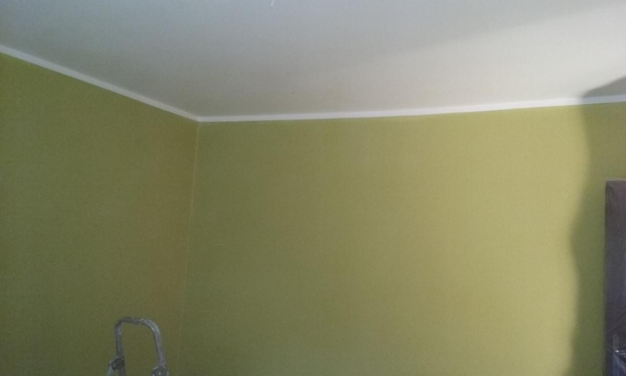 Ściana pomalowana na oliwkowy kolor z białą listwą przy suficie. W rogu widoczny fragment drabiny malarskiej i zasłonięty obiekt.