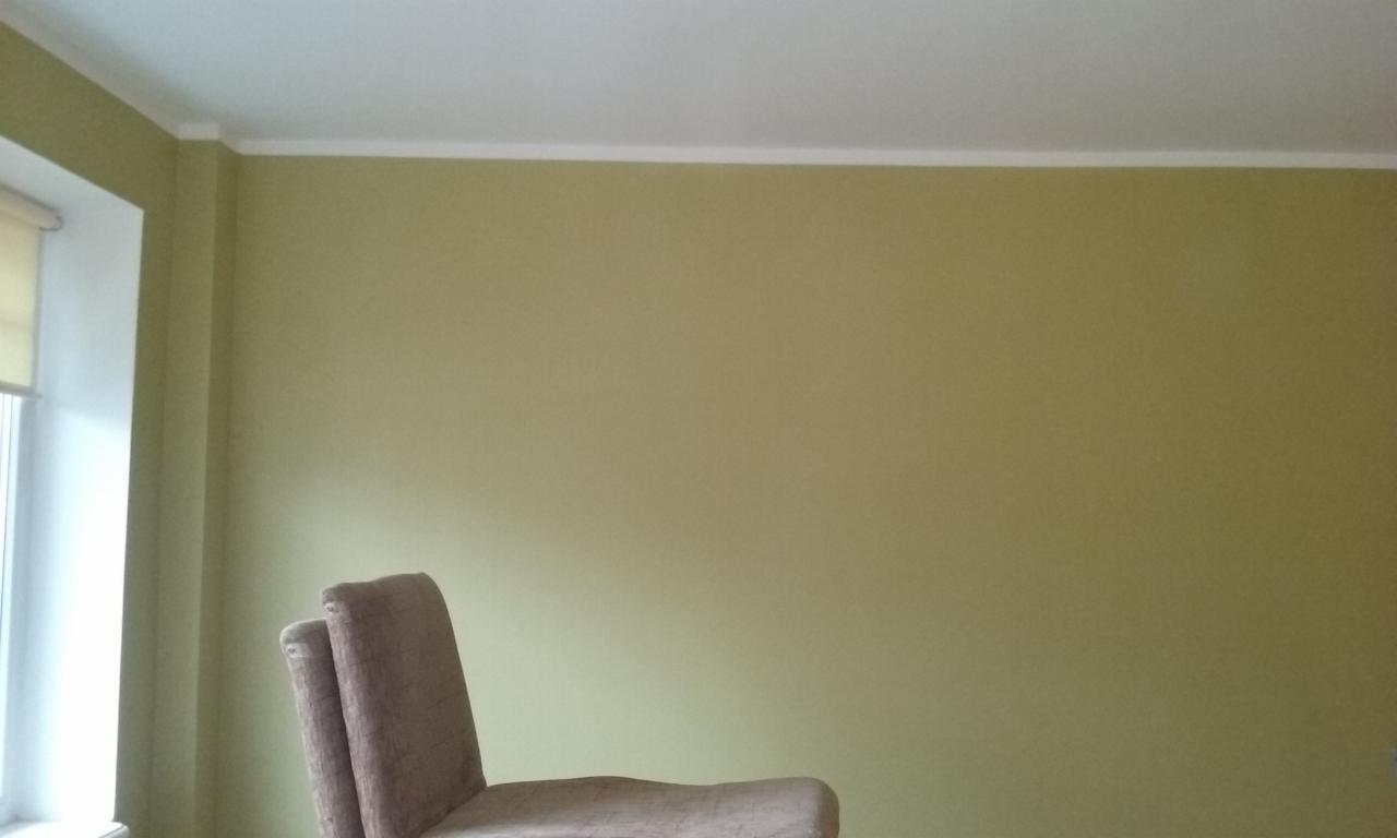 Ściana w odcieniach zieleni po malowaniu, widoczny fragment okna z roletą i krzesło w dolnej części kadru. Listwa dekoracyjna pod sufitem.