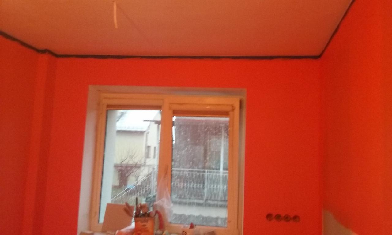 Pomarańczowe ściany w pokoju po malowaniu, widoczne okno i listwa sufitowa. Charakterystyczny odcień farby i wykończenie.