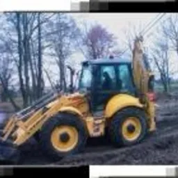 Żółta koparko-ładowarka na nierównym, błotnistym terenie z drzewami w tle, uchwycona w pochmurny dzień.