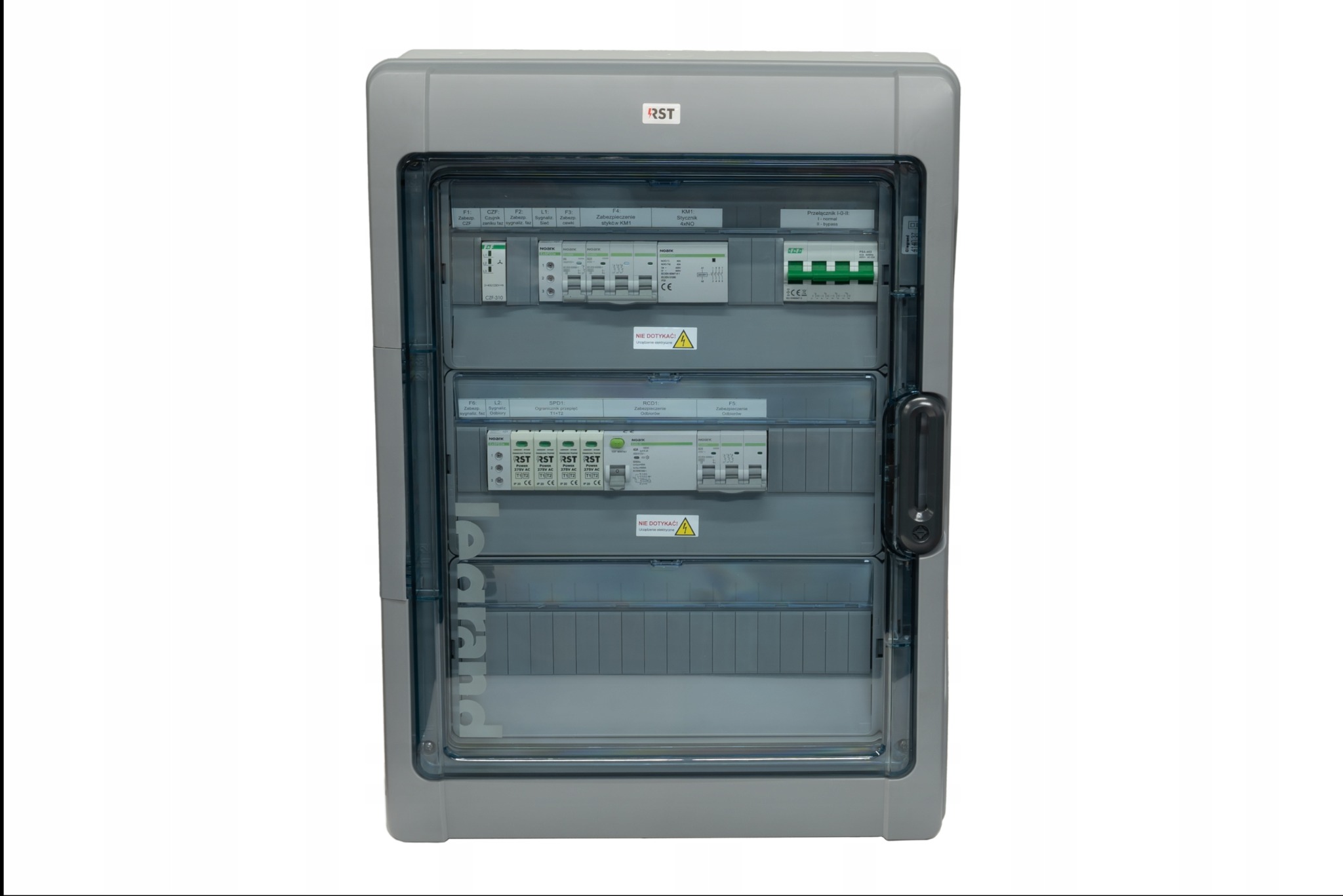 Szara skrzynka elektryczna z przezroczystymi drzwiczkami, widoczne zabezpieczenia, styczniki i przełączniki, etykiety informacyjne wewnątrz.