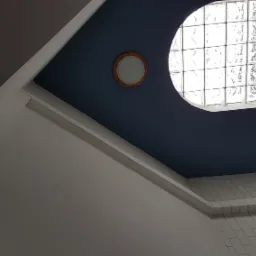 Klatka schodowa z niebieską ścianą, okrągłym oknem z luksferów i lampą w drewnianej oprawie