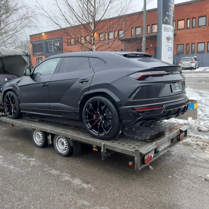 Czarny, matowy Lamborghini Urus na lawecie w Drewnicy, widok z tyłu, z widocznymi czerwonymi zaciskami hamulcowymi i poczekalnią w tle.