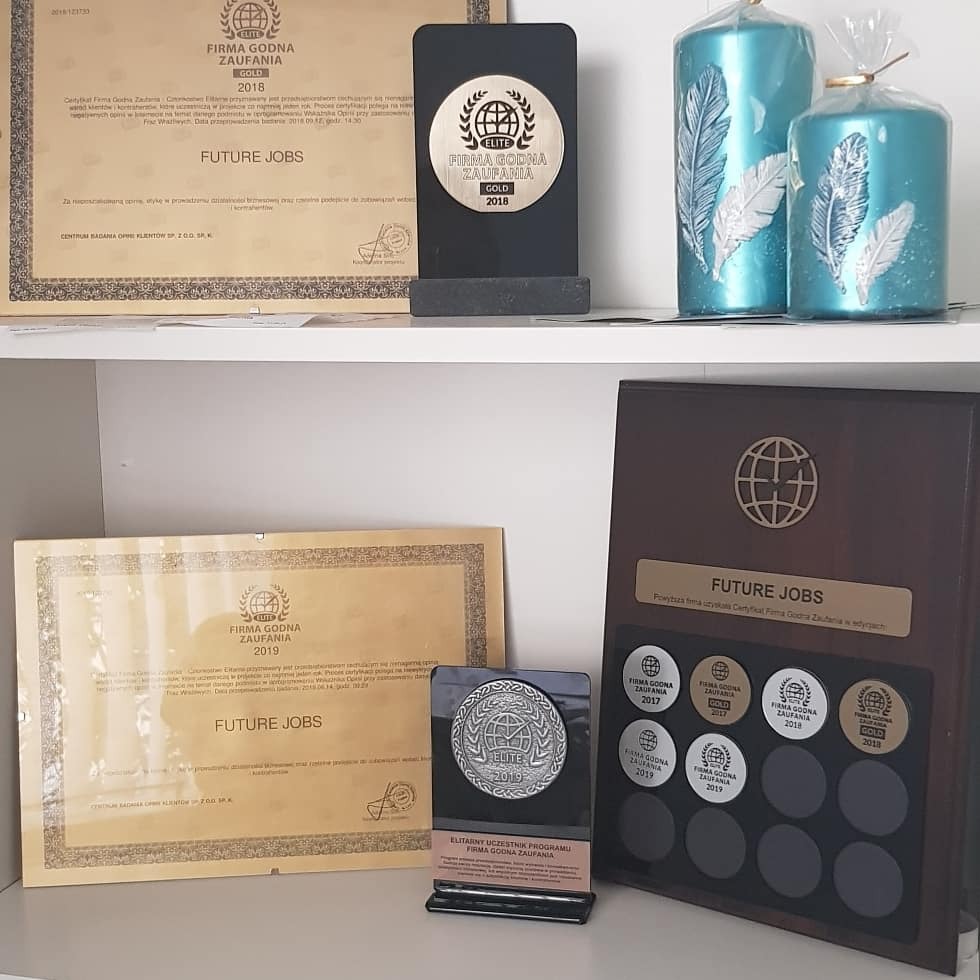 Półka z certyfikatami i nagrodami 'Firma Godna Zaufania' firmy Future Jobs z lat 2017-2019, oraz dwie błękitne świece z motywem piór