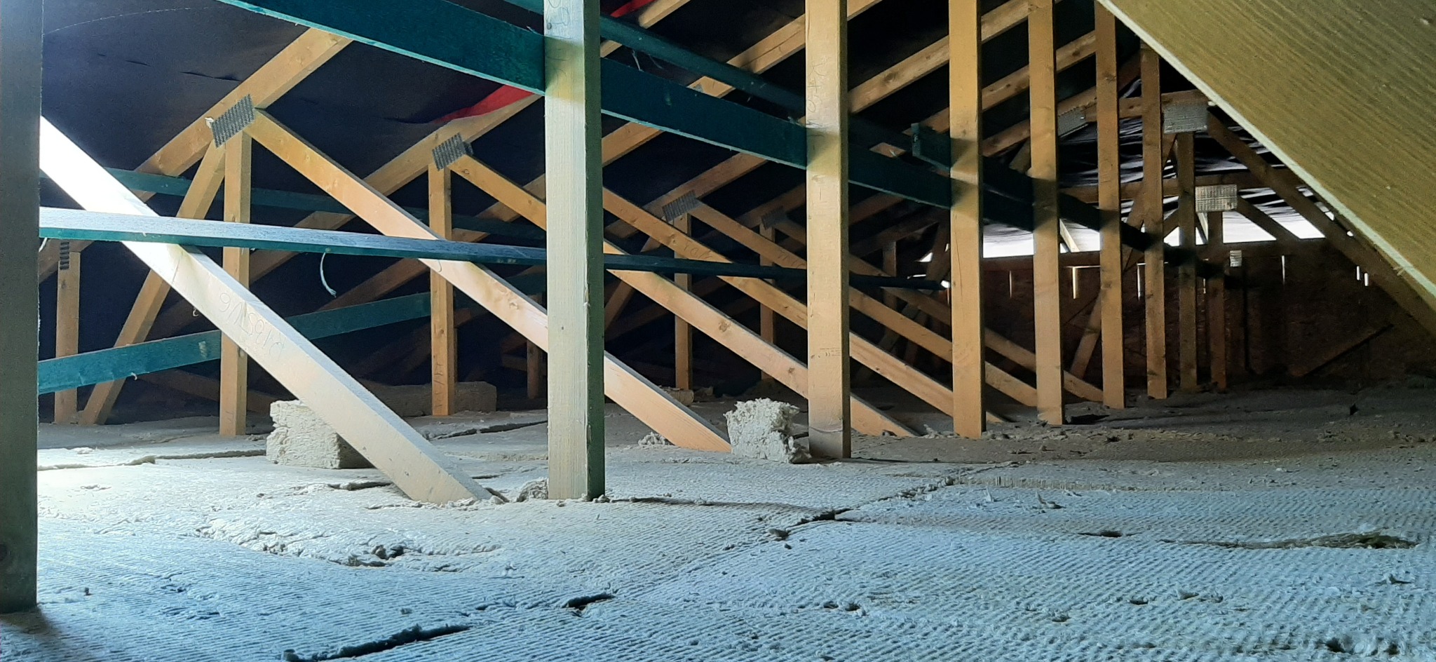 Poddasze z widoczną konstrukcją drewnianą, częściowo pomalowaną na zielono, oraz izolacją z wełny mineralnej na podłodze.