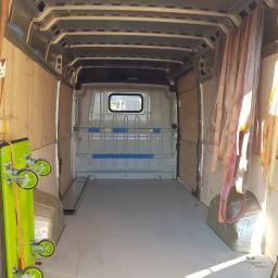 F.H.U DAREK-BUS DARIUSZ MICHALAK - Wnętrze pustego, wyłożonego sklejką busa transportowego z zabezpieczeniami ładunku, widok z tyłu pojazdu.