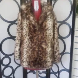 Damskie futro z kapturem w panterkę prezentowane na czerwonym manekinie krawieckim na tle parawanu z geometrycznym wzorem.