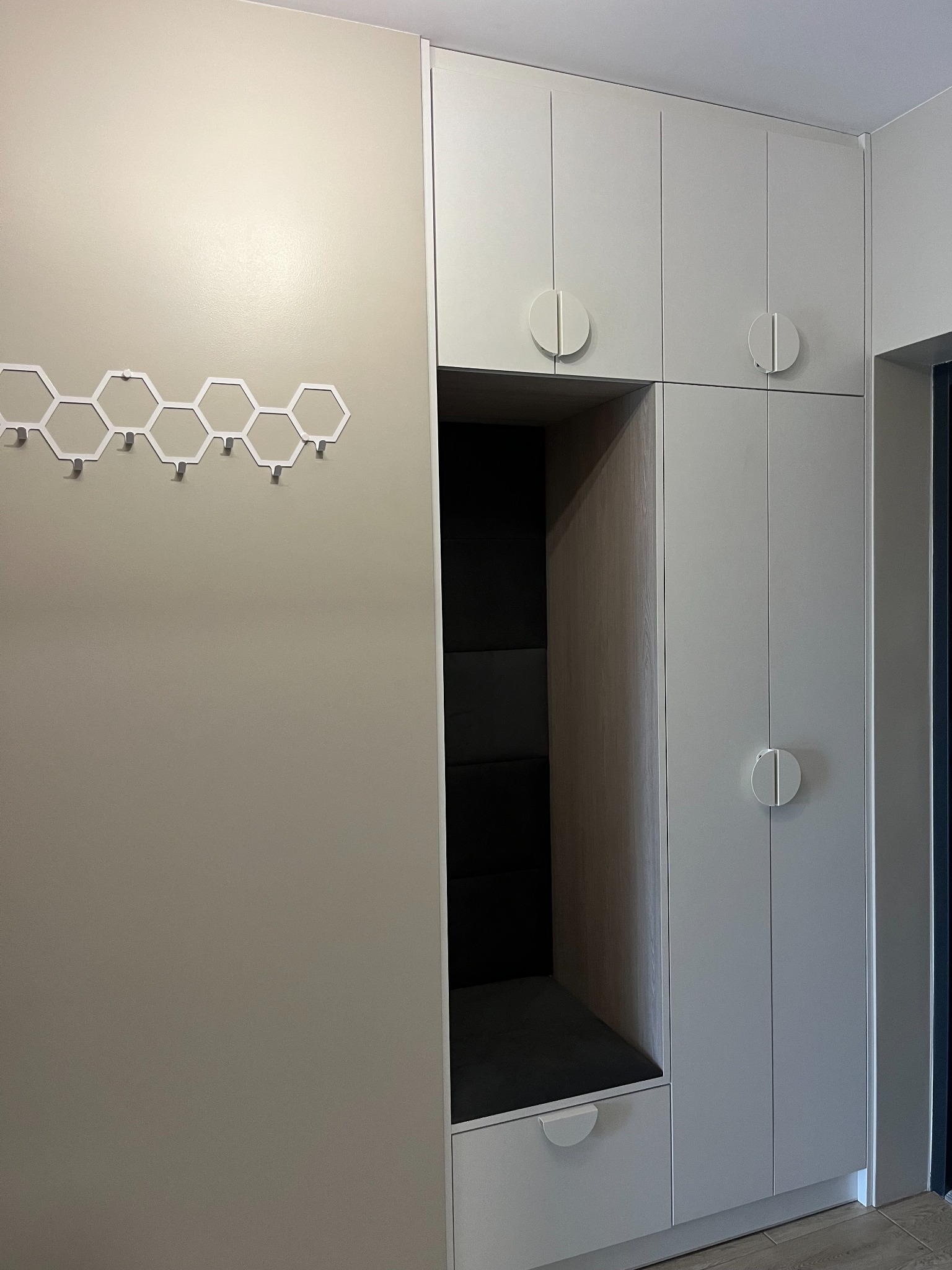 Wnęka z siedziskiem i szafkami w przedpokoju w odcieniach szarości, z wieszakiem ściennym o heksagonalnym wzorze.