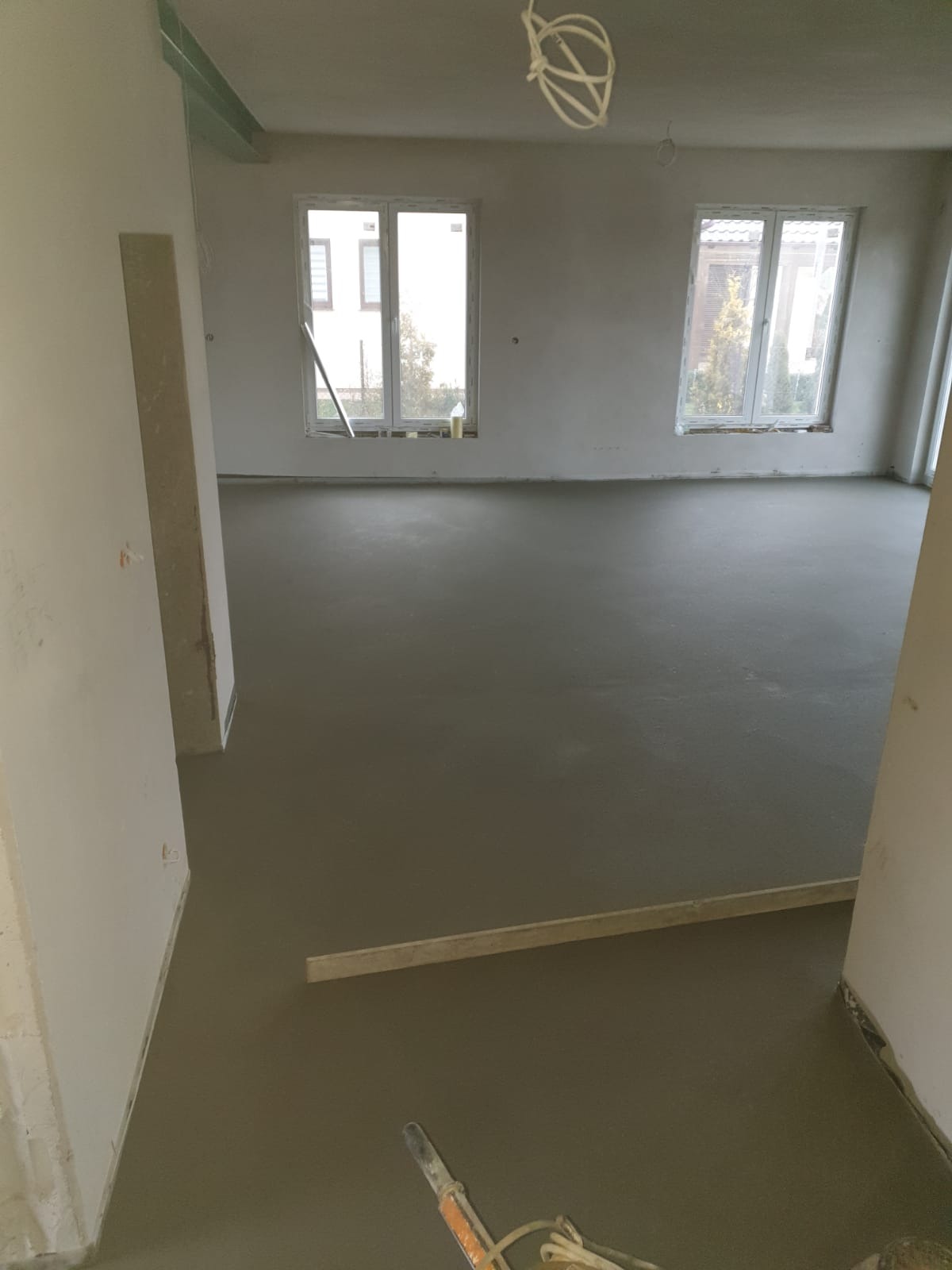 Świeżo wylana, gładka posadzka jastrychowa w jasnym pomieszczeniu z dwoma oknami, widoczna poziomica i narzędzia.