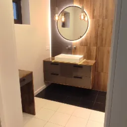 Nowoczesna łazienka z podświetlanym lustrem, wiszącą szafką z szufladami i białymi płytkami podłogowymi.