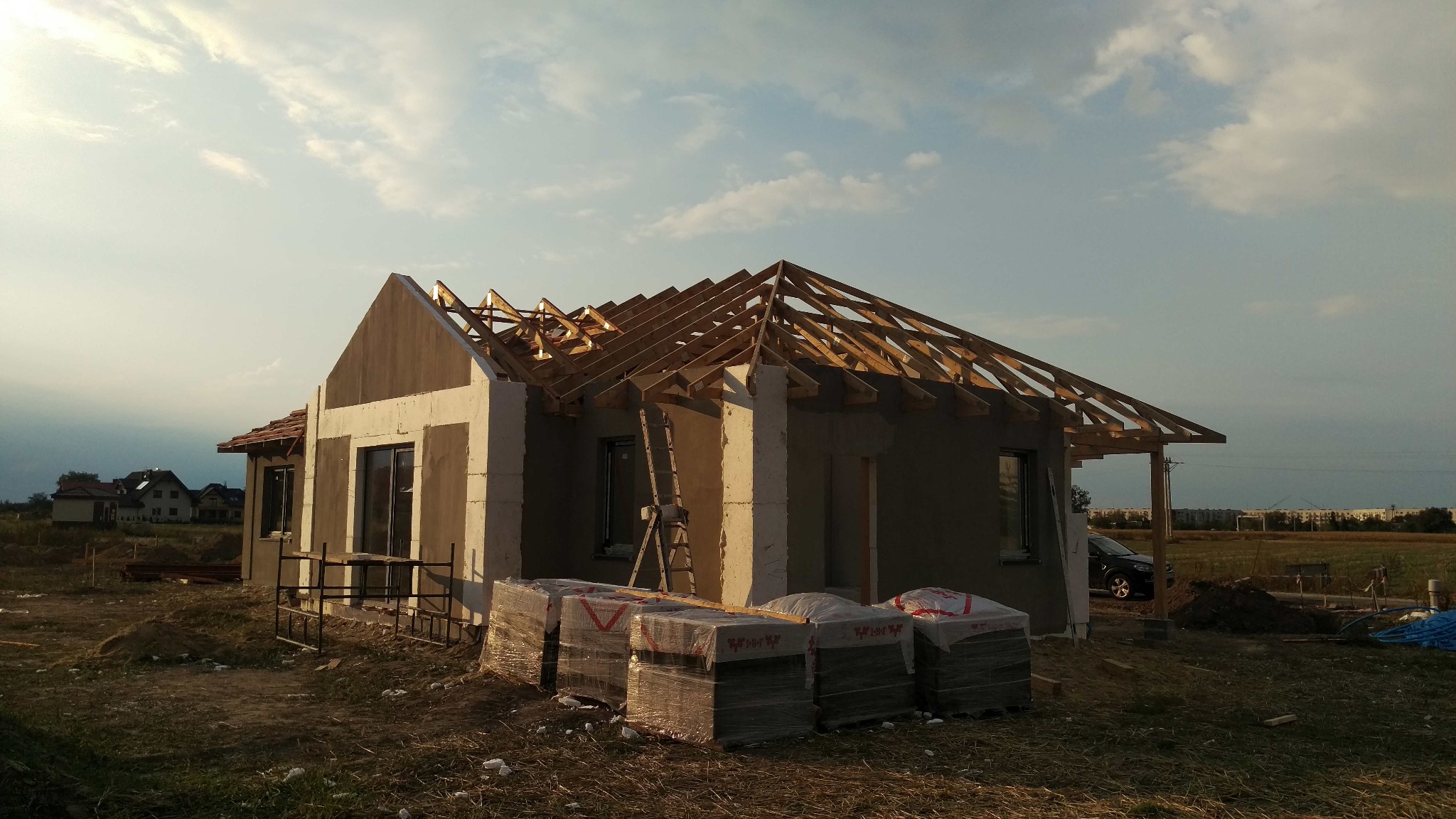 Budowa domu jednorodzinnego w trakcie montażu więźby dachowej, widoczne bloczki budowlane i drabina oparta o ścianę.