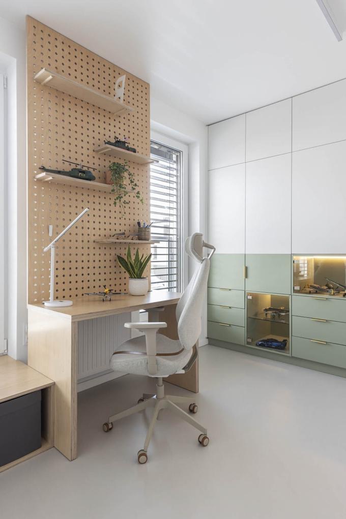 Nowoczesny pokój z biurkiem z drewnianą ścianką z otworami, na której umieszczone są półki z dekoracjami. Krzesło biurowe i zabudowa meblowa w tle.